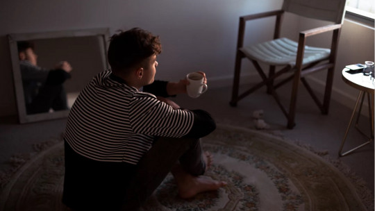 Adolescente sentado en el suelo de una habitación.